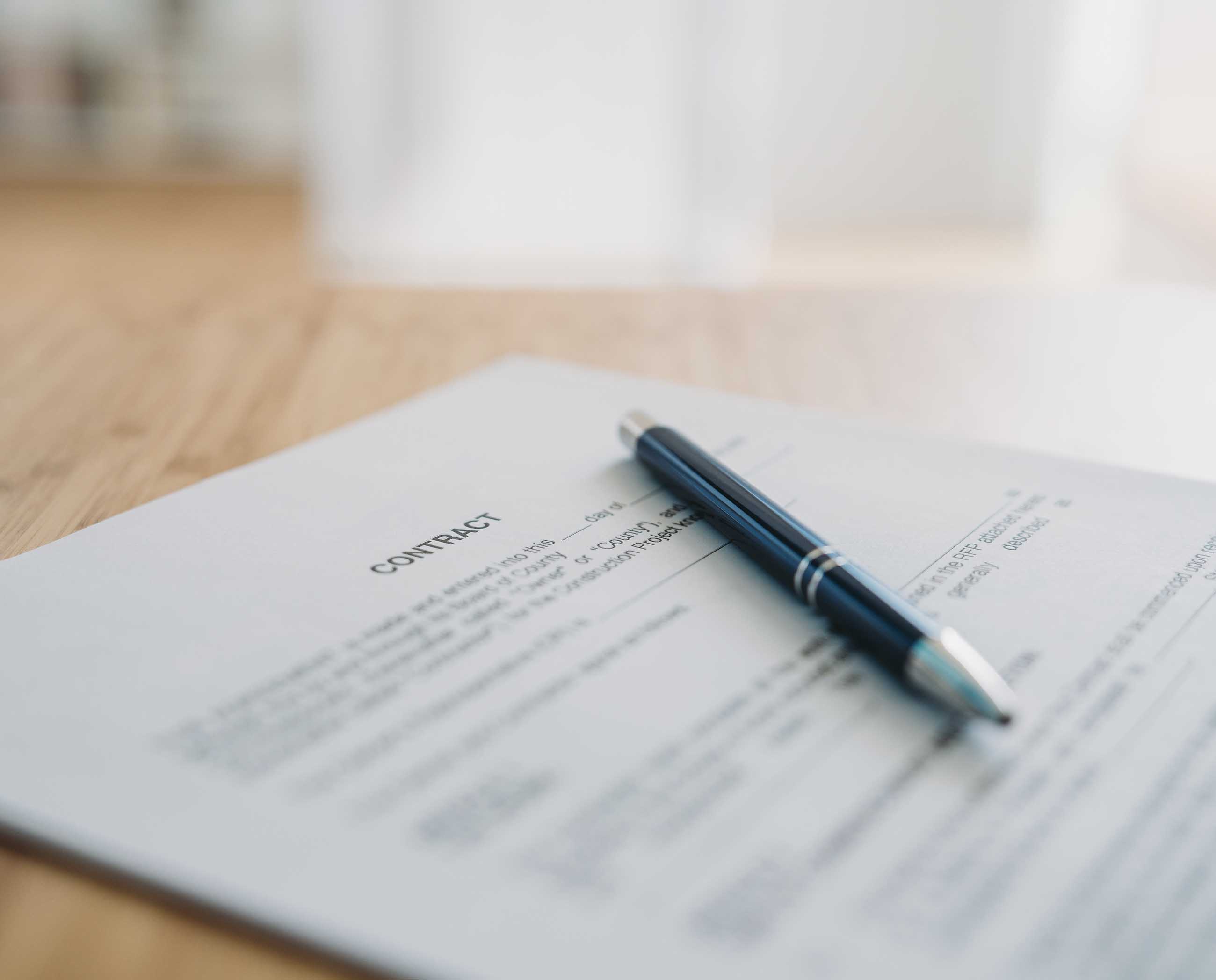 a pen and contract document on top of a wooden table